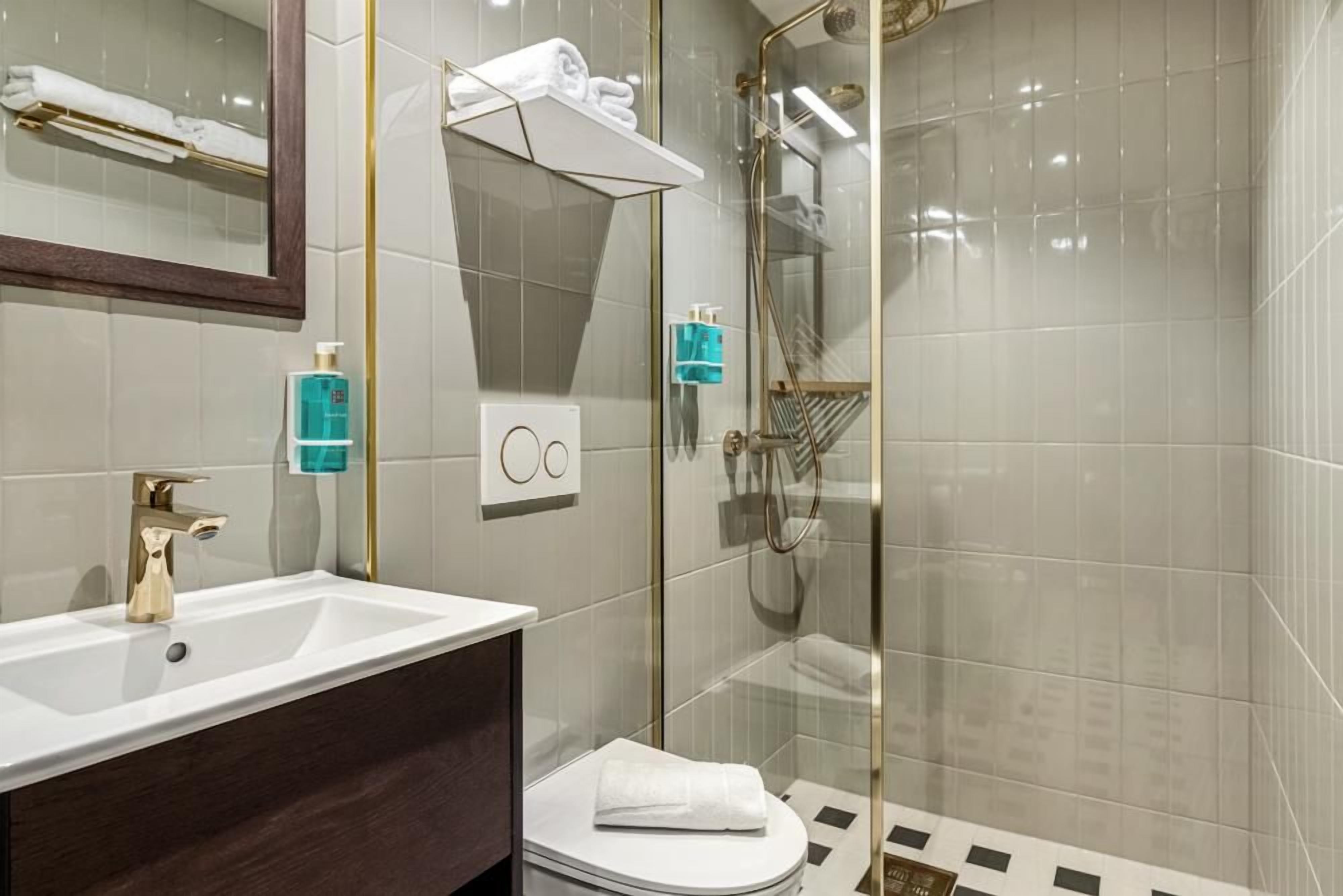 Une salle de bain moderne avec un lavabo blanc, un robinet doré et une cabine de douche en verre.