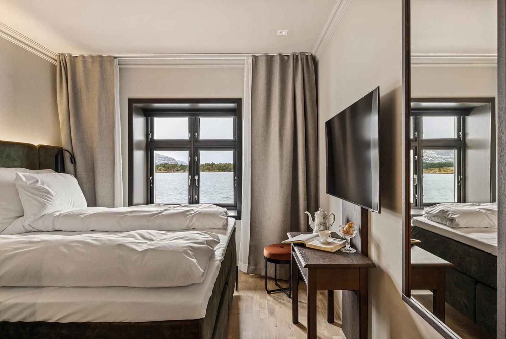 Une chambre d’hôtel avec deux lits, un bureau avec une chaise, une télévision et de grandes fenêtres donnant sur un lac.