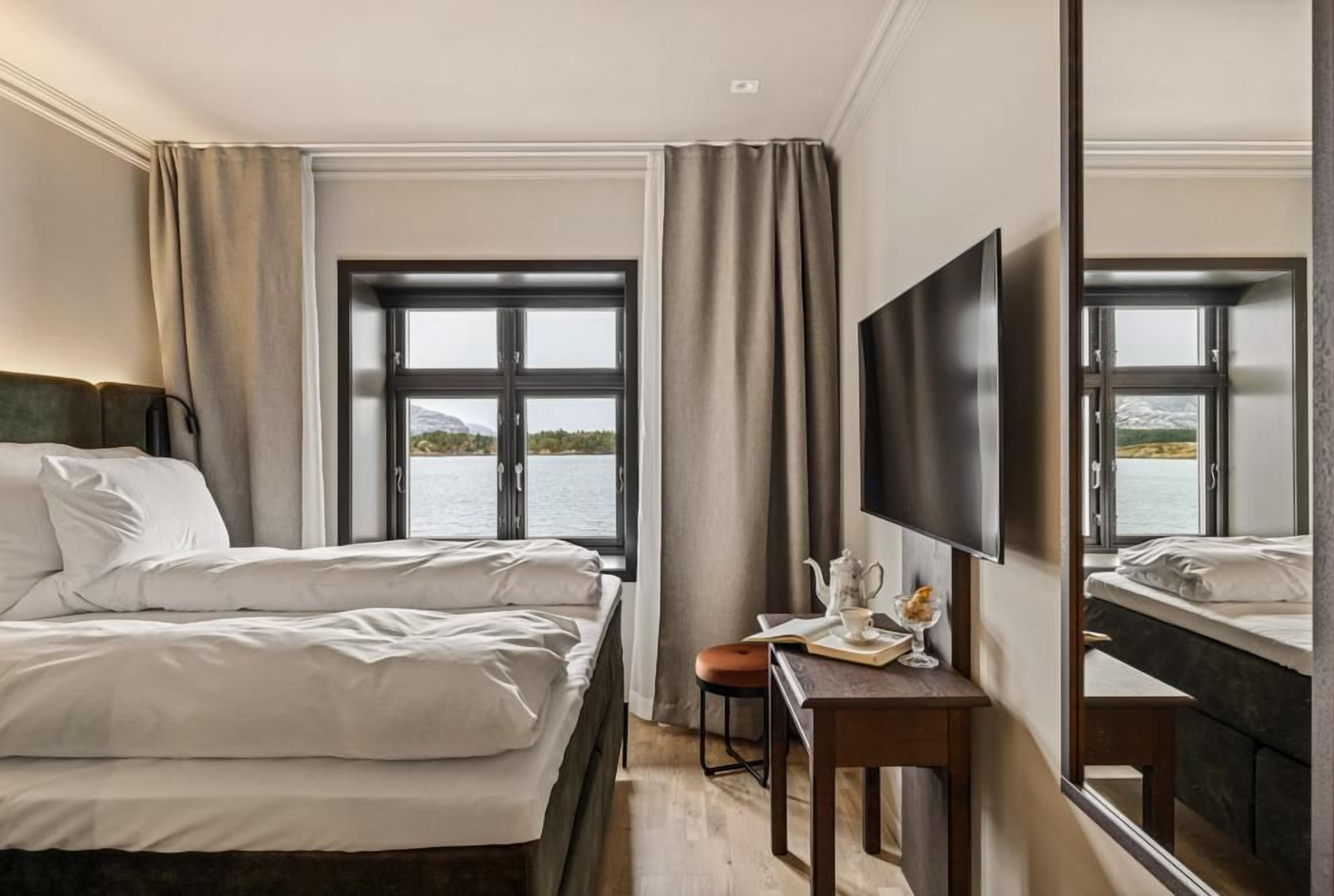 Une chambre d’hôtel dotée d’un grand lit, d’un bureau avec une chaise, d’une télévision à écran plat et d’une grande fenêtre donnant sur l’eau.