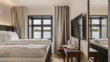 Une chambre d’hôtel dotée d’un grand lit, d’un bureau avec une chaise, d’une télévision à écran plat et d’une grande fenêtre donnant sur l’eau.