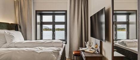 Habitación de hotel con una cama grande, un escritorio con silla, un televisor de pantalla plana y un ventanal con vistas al agua.