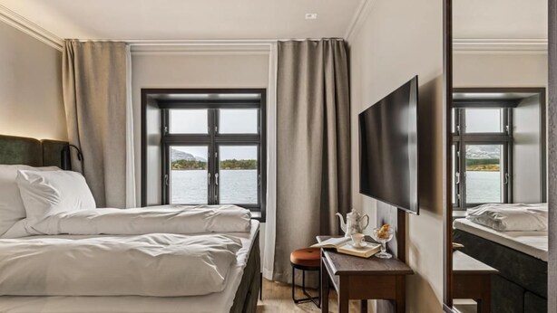 A hotel room with a large bed, a desk with a chair, a flat-screen TV, and a large window offering a view of the water. - Biologen Hotel (Askøy)