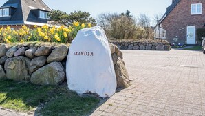 Ein Steinschild mit der Aufschrift "SKANDIA", eine Steinmauer und eine gepflasterte Fläche mit Häusern im Hintergrund.