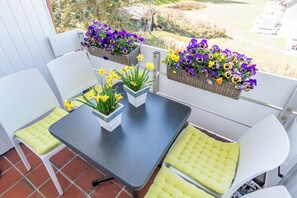 Ein Balkon mit Tisch, Stühlen, Topfpflanzen und hängenden Blumenkörben.