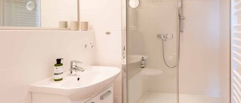 Un baño moderno con ducha envuelta en vidrio, un lavabo blanco y un espejo sobre él.