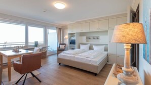 A modern hotel room with a large bed, a desk, and a dining area. - 1-zimmerwohnung mit Meerblick und ca. 46 m² Wohnfläche, für bis zu 2 Personen (Wenningstedt-Braderup (Sylt))