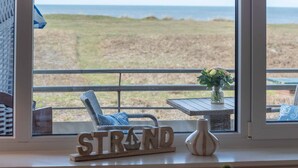 A view from a balcony with a wicker chair, a small table with a vase of flowers, and a sign that reads "STRAND". - 1-zimmerwohnung mit Meerblick und ca. 46 m² Wohnfläche, für bis zu 2 Personen (Wenningstedt-Braderup (Sylt))