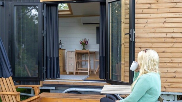 Una cabaña de madera con una puerta corredera abierta, un banco de madera y una mesa afuera.