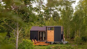 Una cabaña pequeña con terraza de madera y techo de metal, rodeada de árboles.