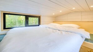 Un dormitorio con cama, ventana y techo de madera.