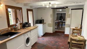Een kleine keuken met een wasmachine, een spoelbak en een eethoek met stoelen en een tafel.