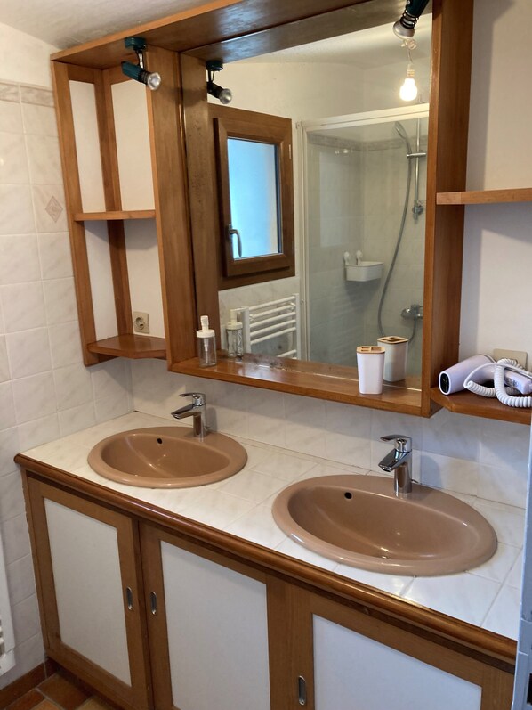 Un baño con dos lavamanos, un espejo y una ducha visible a través de una puerta de cristal.