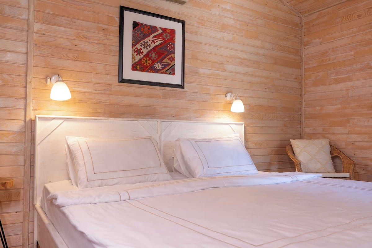 A wooden-paneled room with a bed, two wall-mounted lamps, and a framed artwork.