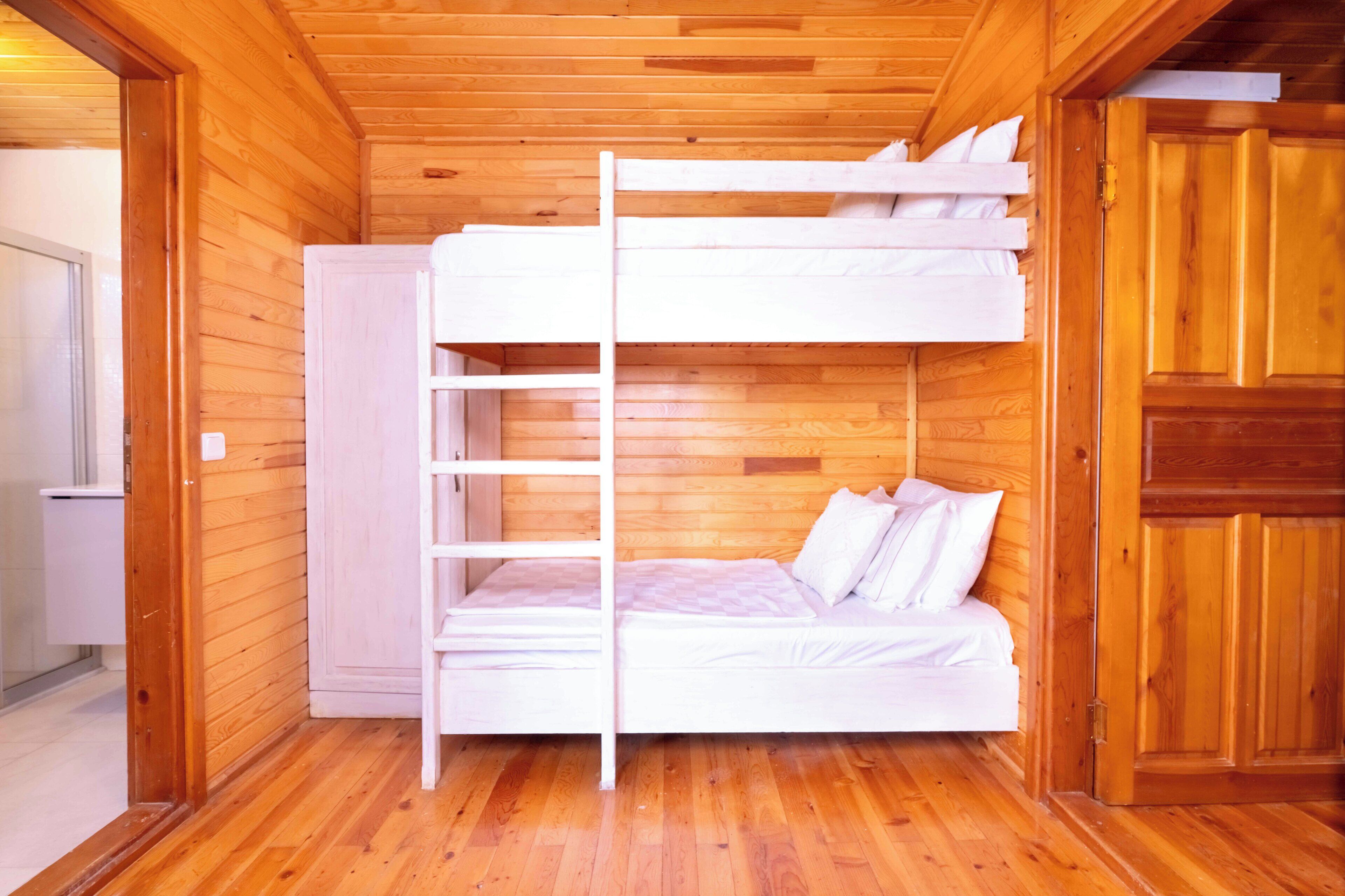 A bunk bed room with wooden walls and floors, a white bed, and a ladder.