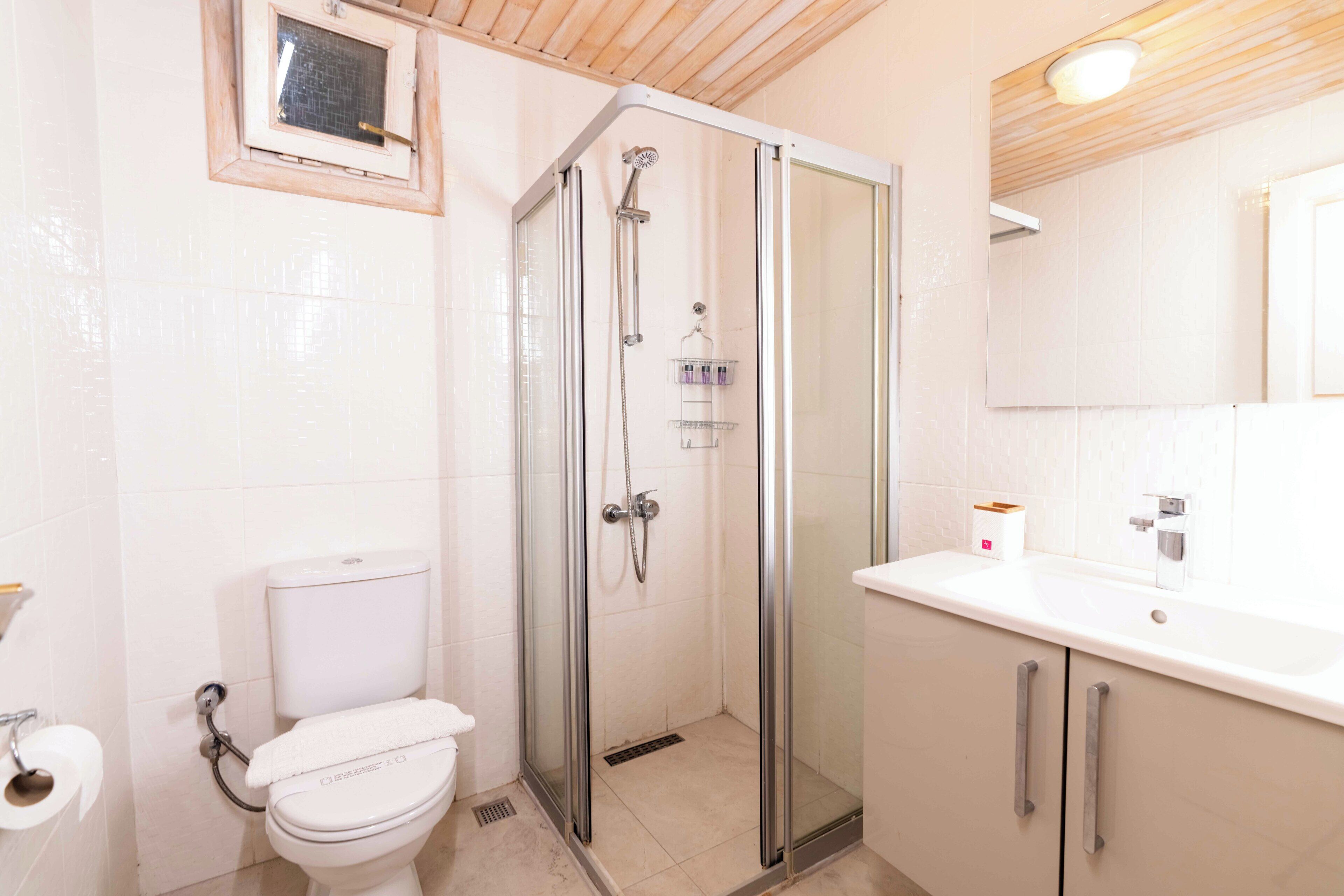 A modern bathroom with a glass-enclosed shower, a toilet, and a sink with a mirror above.