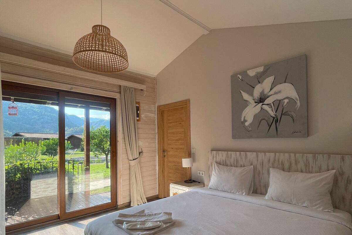 A spacious bedroom with a large bed, a view of the outdoors, and a ceiling light.