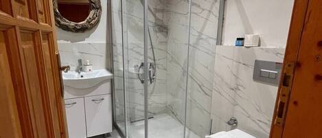 Un baño con cabina de ducha de vidrio, inodoro, lavabo y techo de madera.