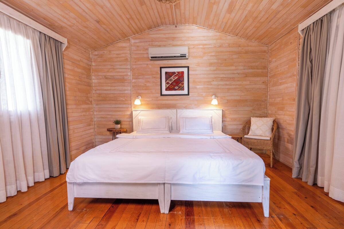 A wooden-paneled room with a bed, curtains, a wall-mounted air conditioner, and a framed picture.
