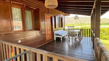 A wooden deck with a table and chairs, a hanging light fixture, and a view of greenery.
