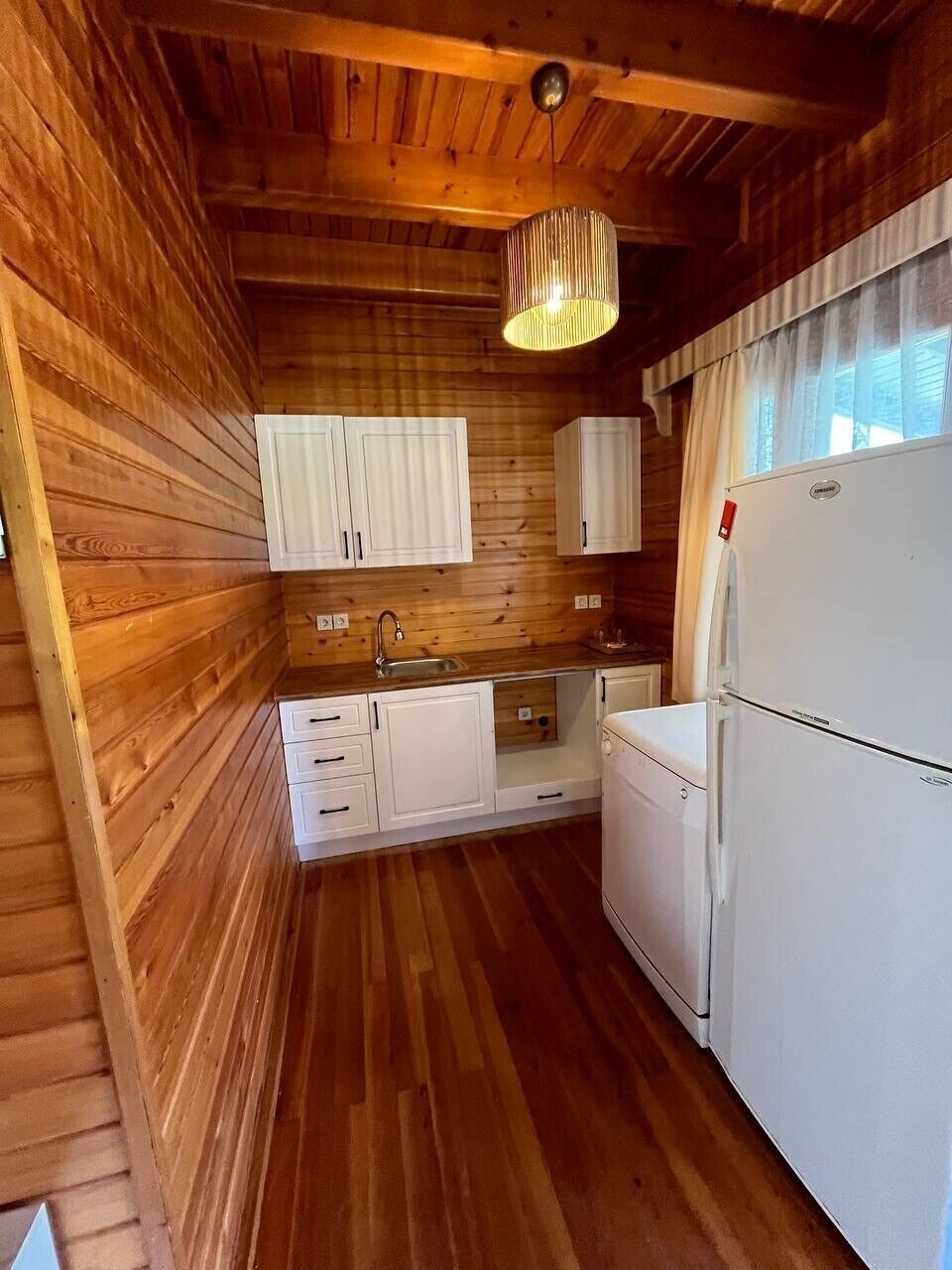 A compact kitchen with wooden walls, white cabinets, a sink, and a refrigerator.