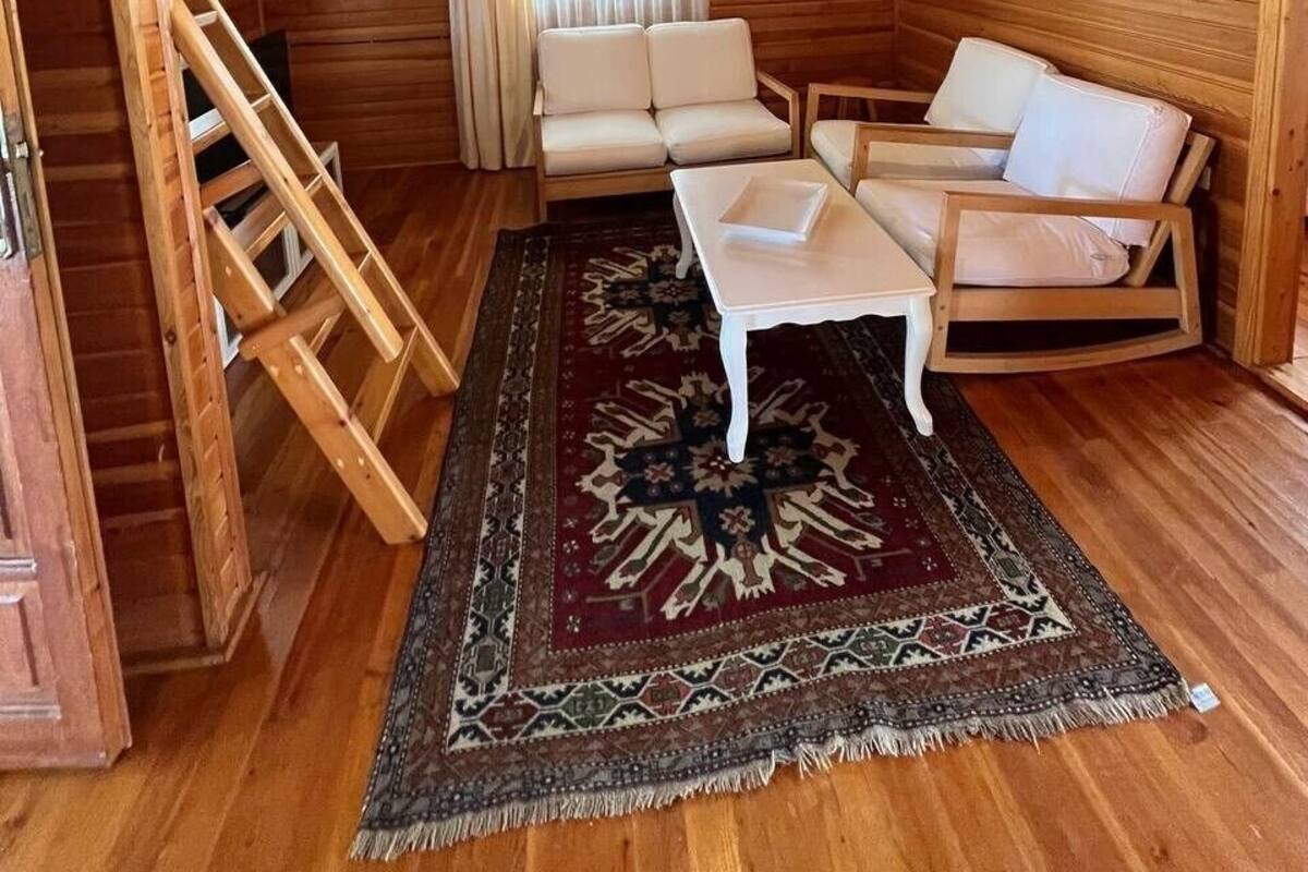 A log cabin interior with a wooden staircase, a sofa set, a patterned rug, and a hanging light fixture.
