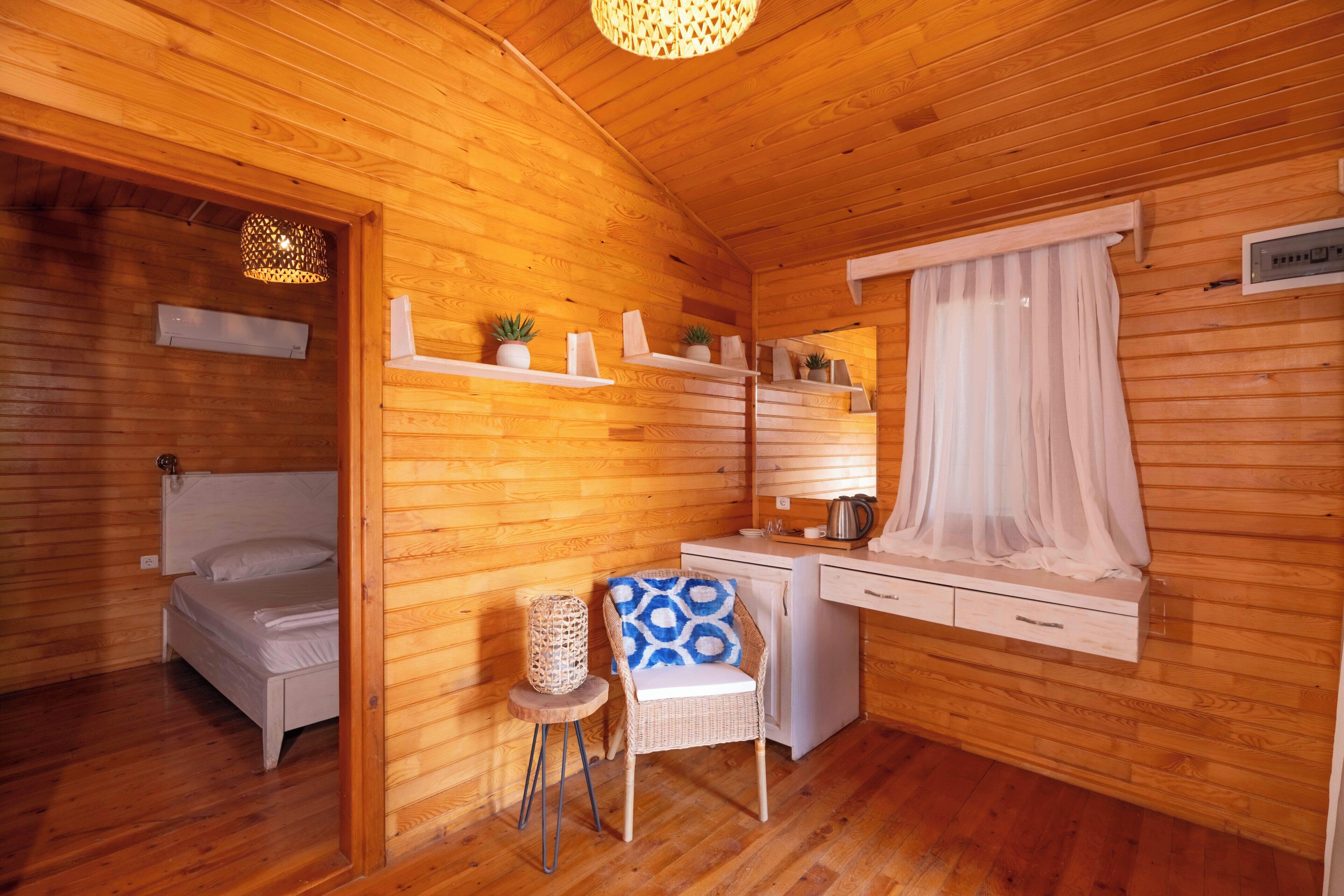 Una habitación acogedora de cabaña de madera, con una cama, un escritorio, una silla y un ventanal con cortina translúcida.