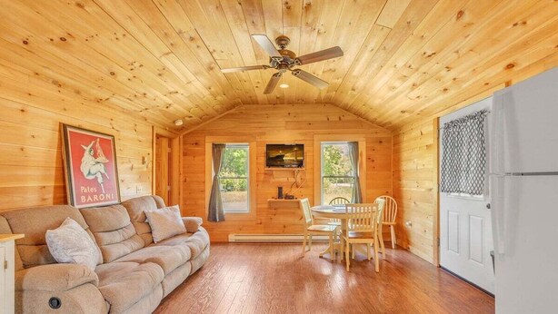 A log cabin interior with a sofa, dining table, chairs, a ceiling fan, and a television. - Seawall Retreat! Close to Ocean & Acadia! (Southwest Harbor)