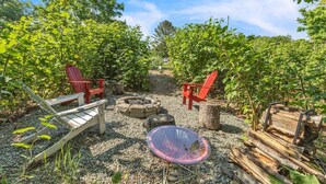 A garden with red Adirondack chairs, a woven chair, and a fire pit. - Seawall Retreat! Close to Ocean & Acadia! (Southwest Harbor)