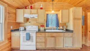 A wooden cabin interior with a kitchen featuring wooden cabinets, a stove, a sink, and a window with curtains. - Seawall Retreat! Close to Ocean & Acadia! (Southwest Harbor)