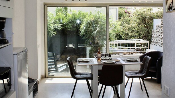 A modern kitchen with a dining area, large sliding glass doors to a garden, and a view of the outdoors. - Garden-Level 2-Room Apartment, 100m from Beach, A/C, Terrace, Free Parking (Villeneuve-Loubet)