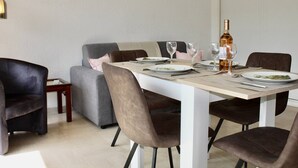 A dining area with a white table, brown chairs, and a grey sofa. - Garden-Level 2-Room Apartment, 100m from Beach, A/C, Terrace, Free Parking (Villeneuve-Loubet)