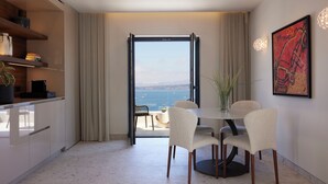 Un comedor moderno con una mesa redonda y cuatro sillas, vista al mar a través de un ventanal y un cuadro en la pared.