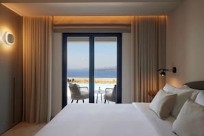 Habitación de hotel con una cama grande, vista al mar y un balcón con mobiliario exterior.