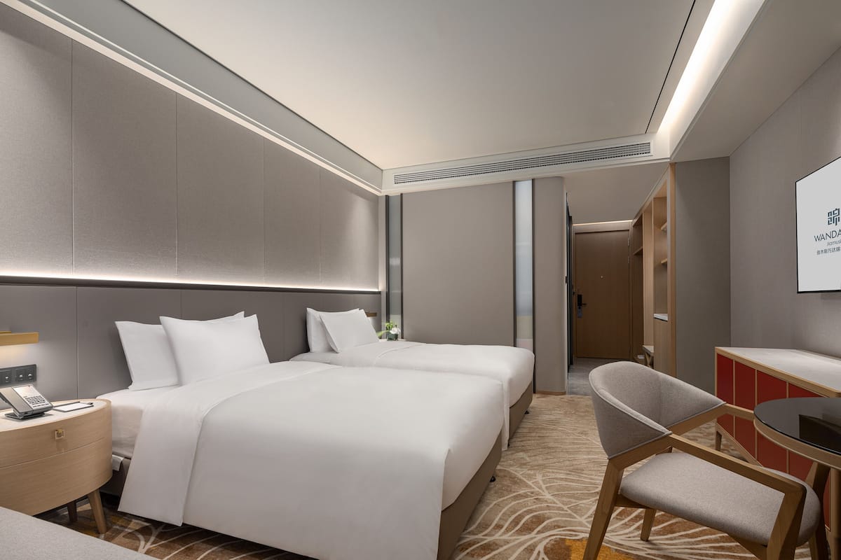 A hotel room with a large bed, a desk with a chair, a small table, and a mirror.