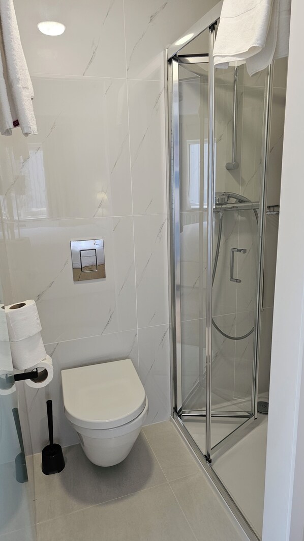 A modern bathroom with a toilet, a glass shower enclosure, and a towel rack.