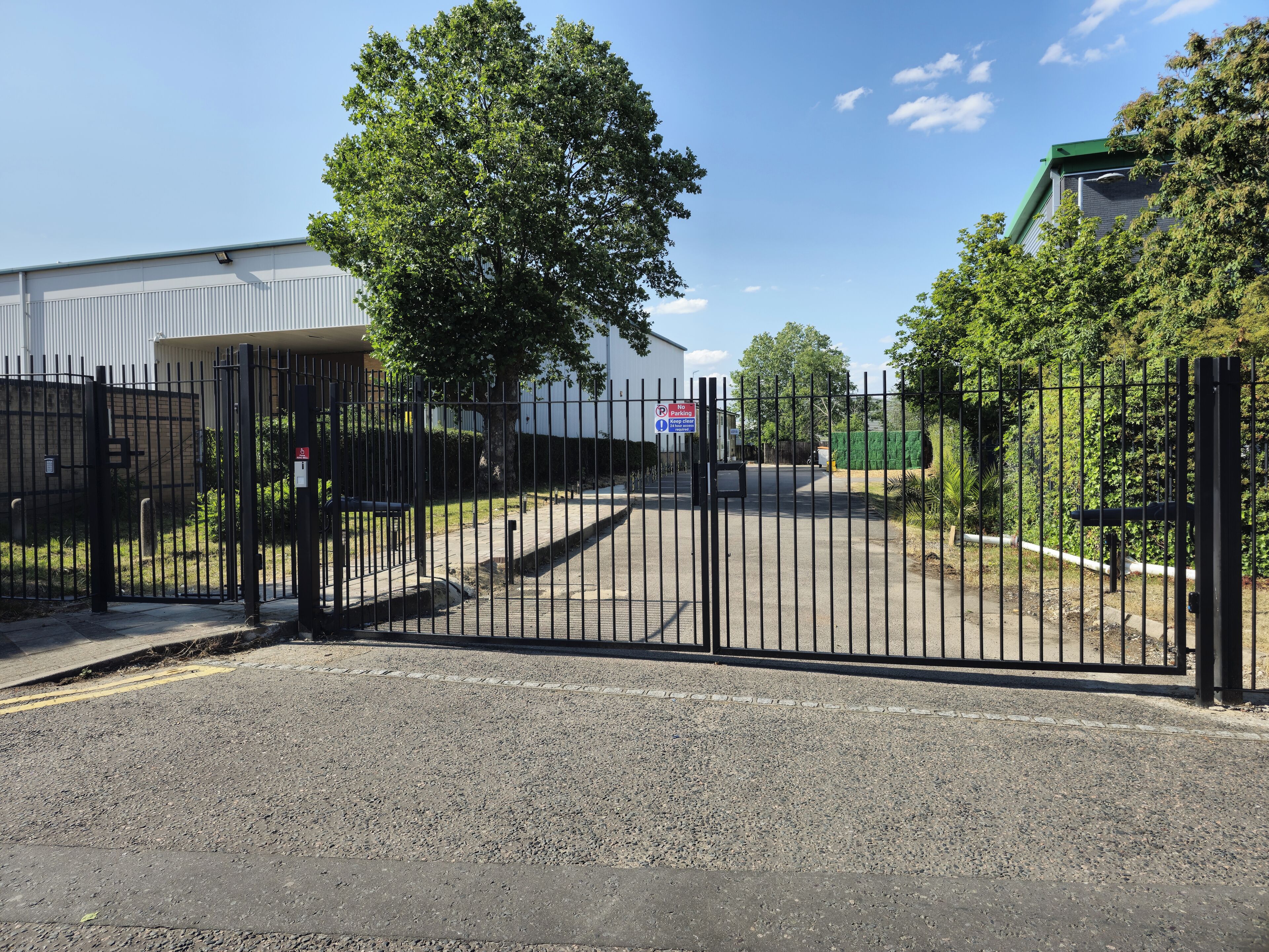 A gated entrance with a no parking sign, a paved driveway, and a building in the background.