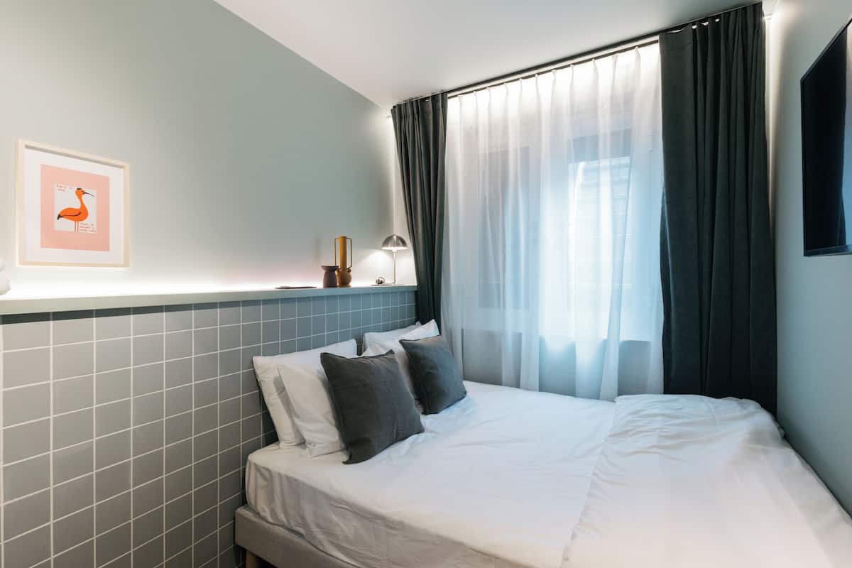 A hotel room with a bed, a nightstand, a framed picture, and a window with curtains.
