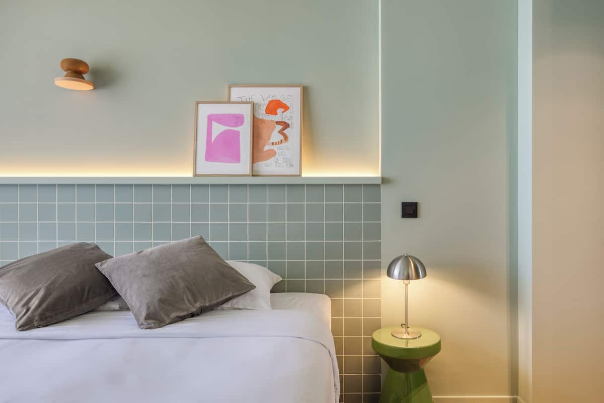 A neatly made bed with two pillows, a bedside lamp, and two framed artworks on the wall.