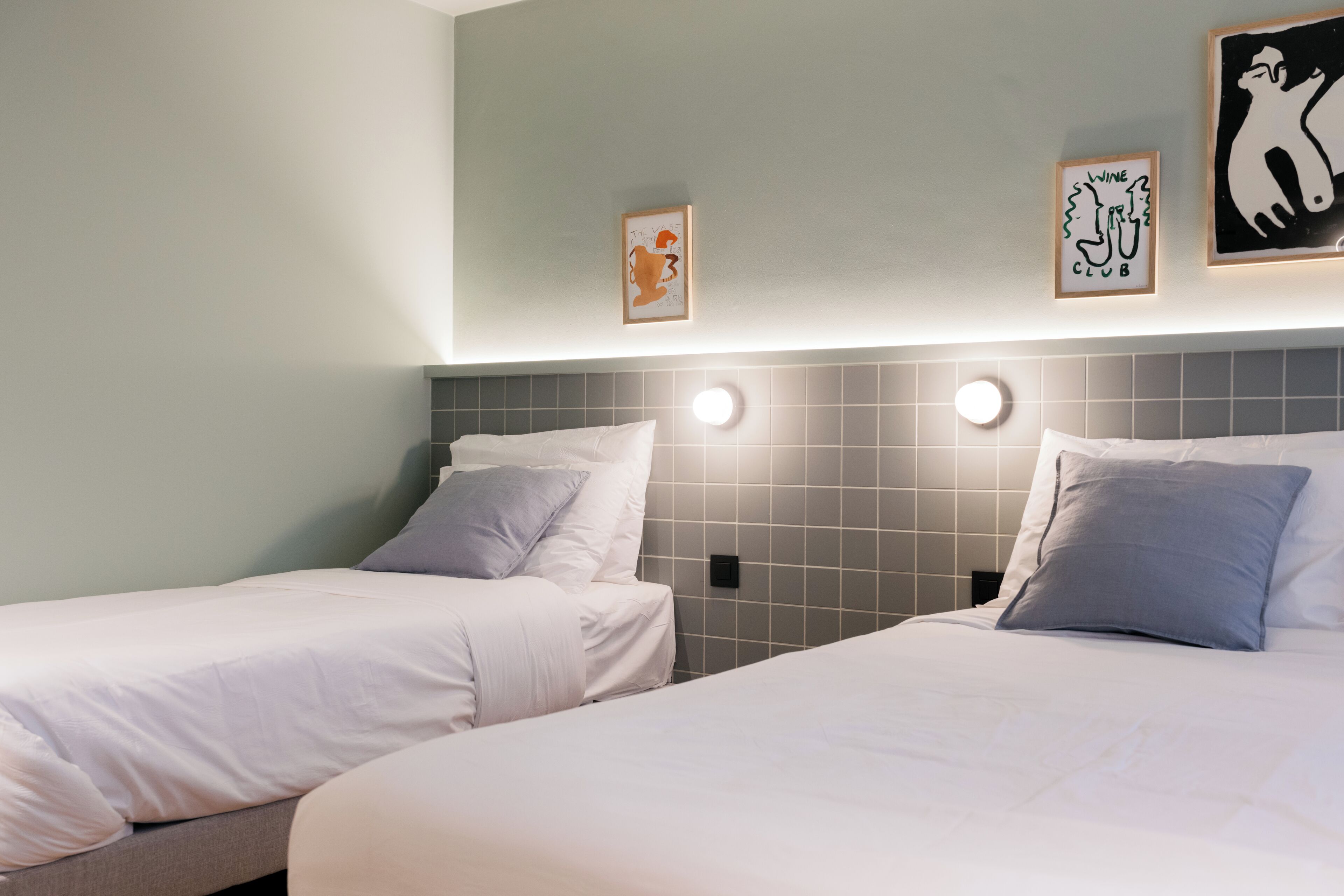 A hotel room with two beds, a tiled headboard, and wall-mounted lights.