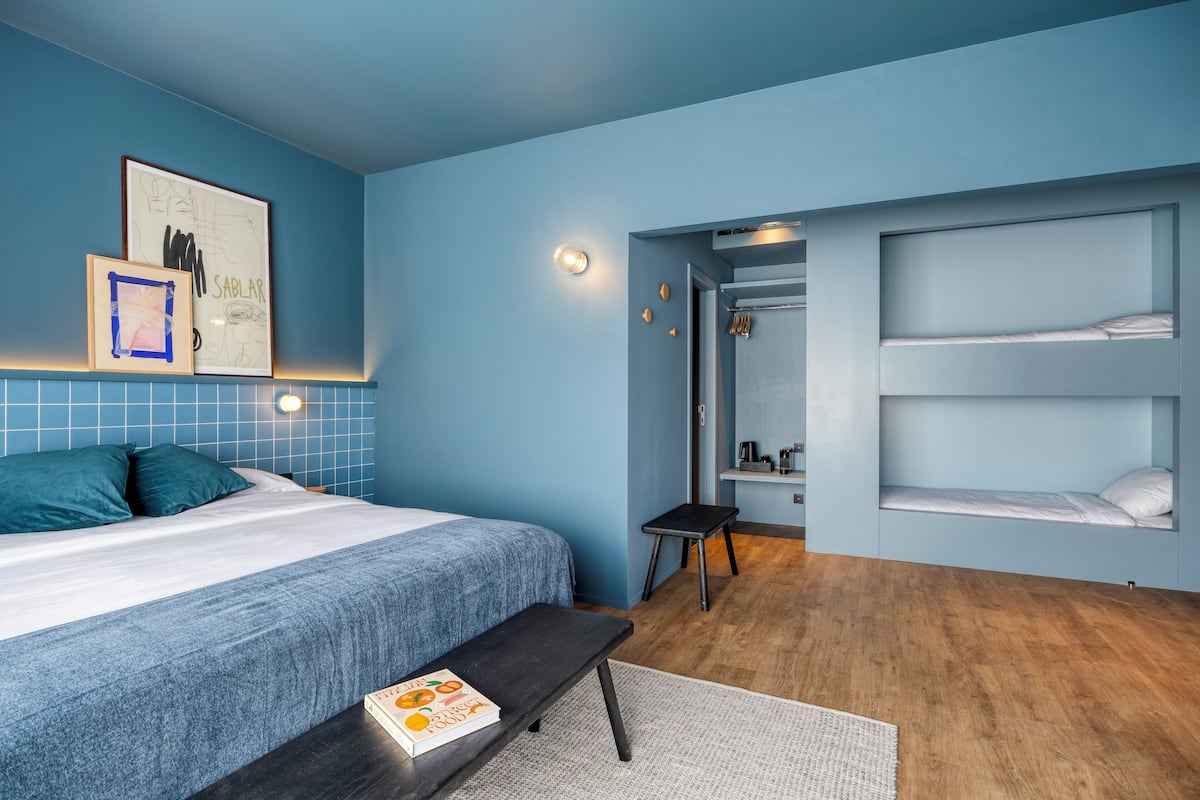 A bedroom with a bed, a bench, a small table with a book, a wardrobe, and a door leading to a bathroom.