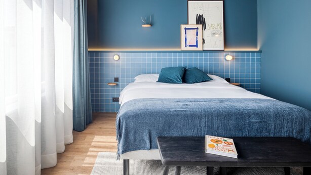 Een moderne slaapkamer met een groot bed, een nachtkastje, een wandlamp en een ingelijst schilderij.