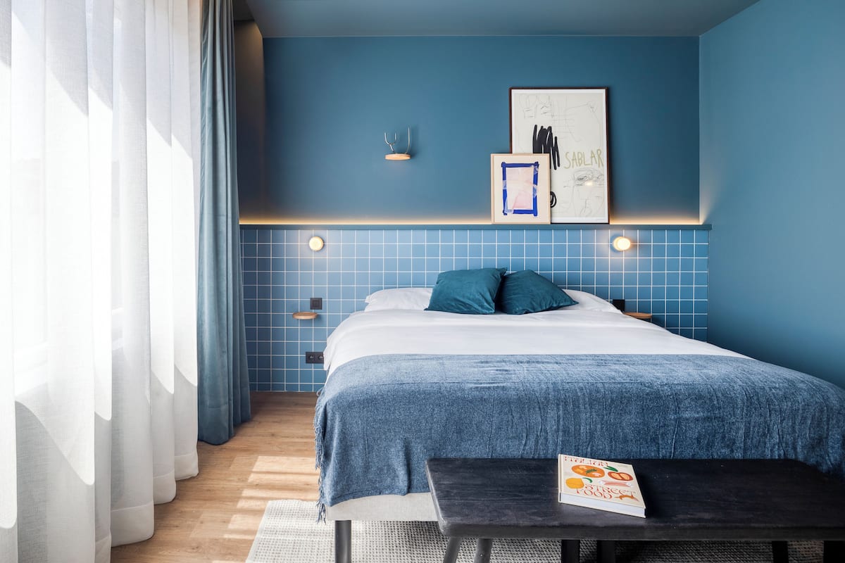 A modern bedroom with a large bed, a bedside table, a wall-mounted light, and a framed picture.