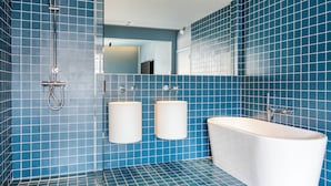 Een badkamer met blauwe betegelde muren, een wit bad en twee wastafels.