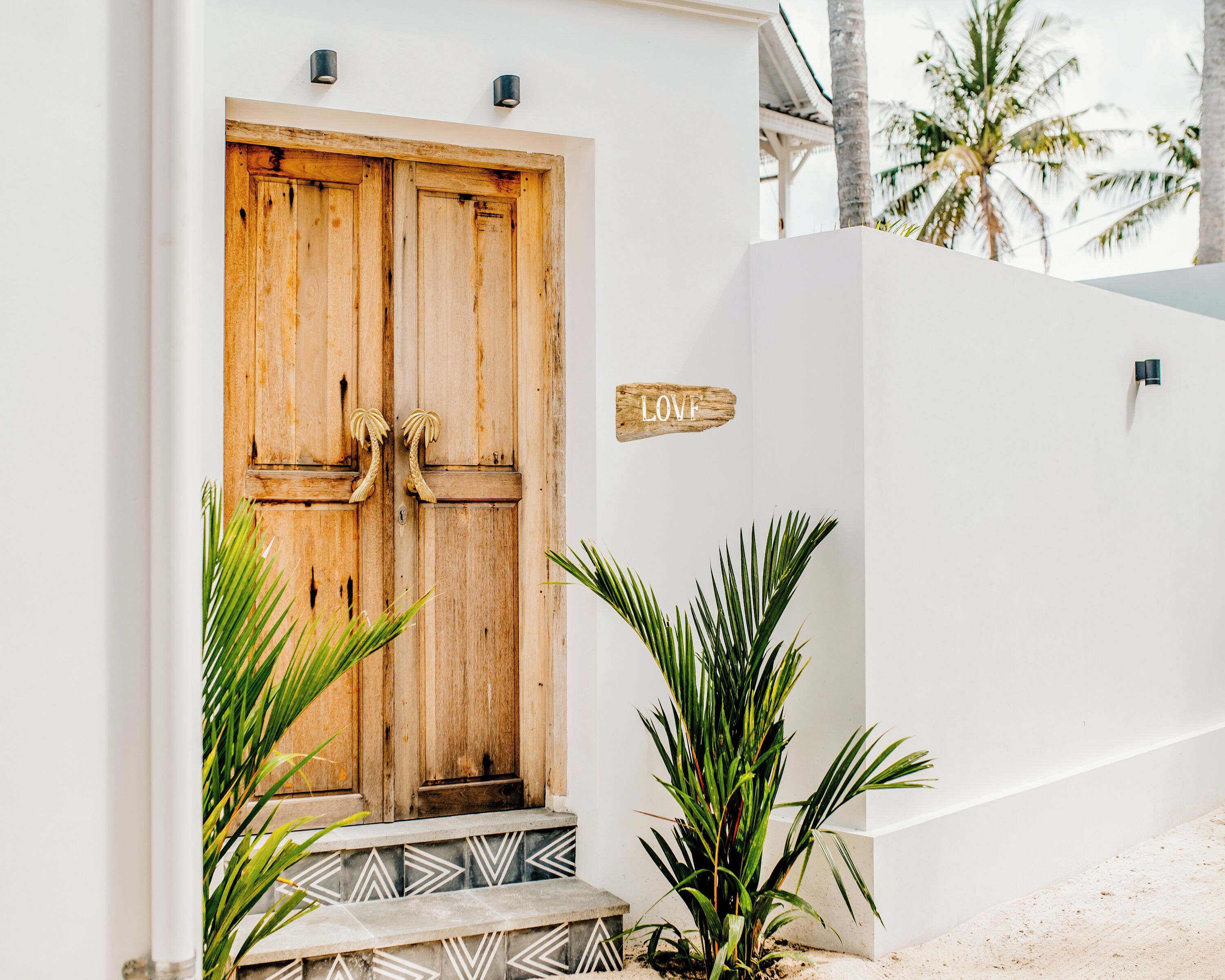 A wooden door with a sign reading "LOVE" above it, a small step leading to the entrance, and a white wall with a small plant beside it.