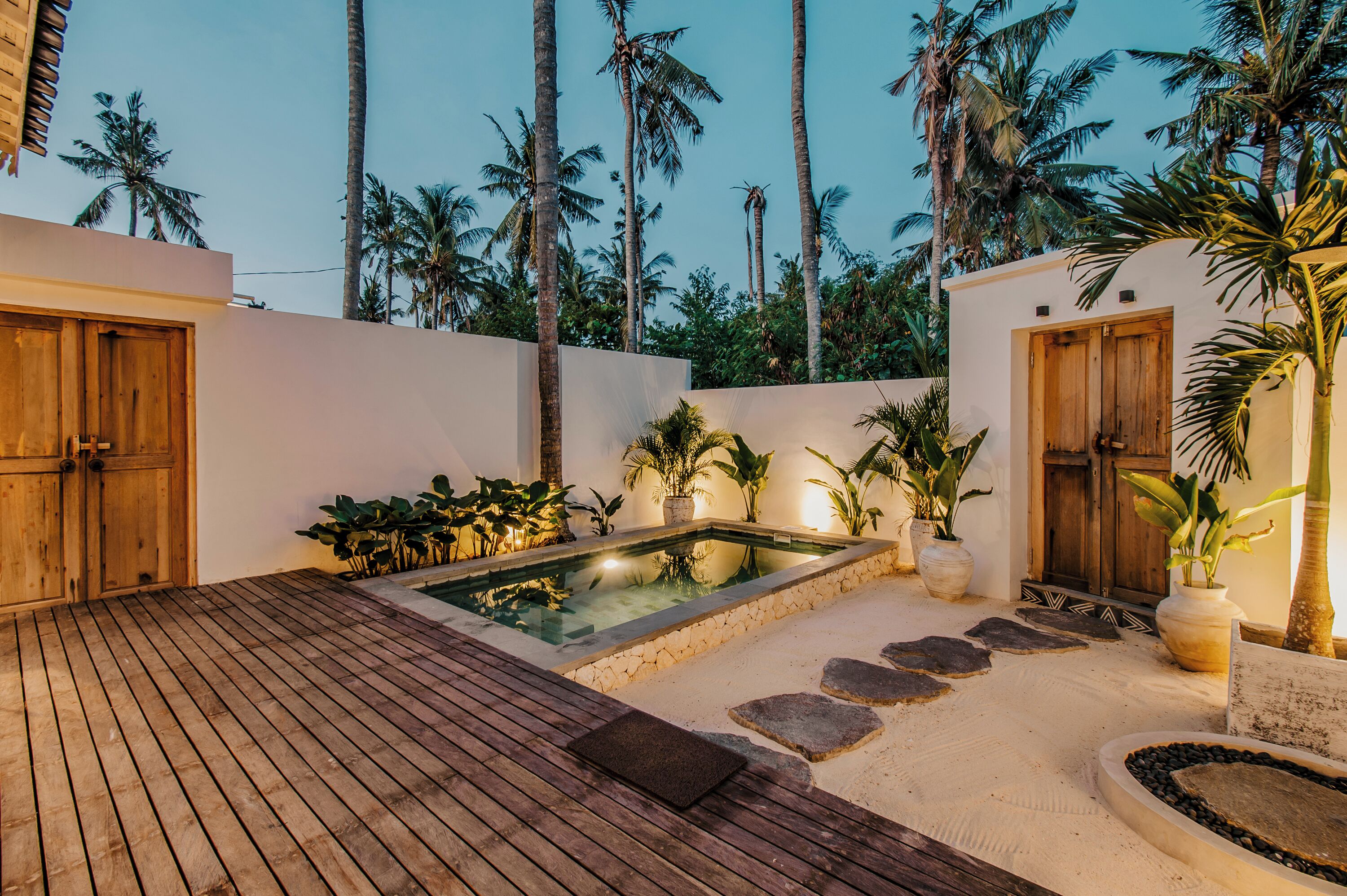 A wooden deck with a swimming pool, surrounded by palm trees and plants.