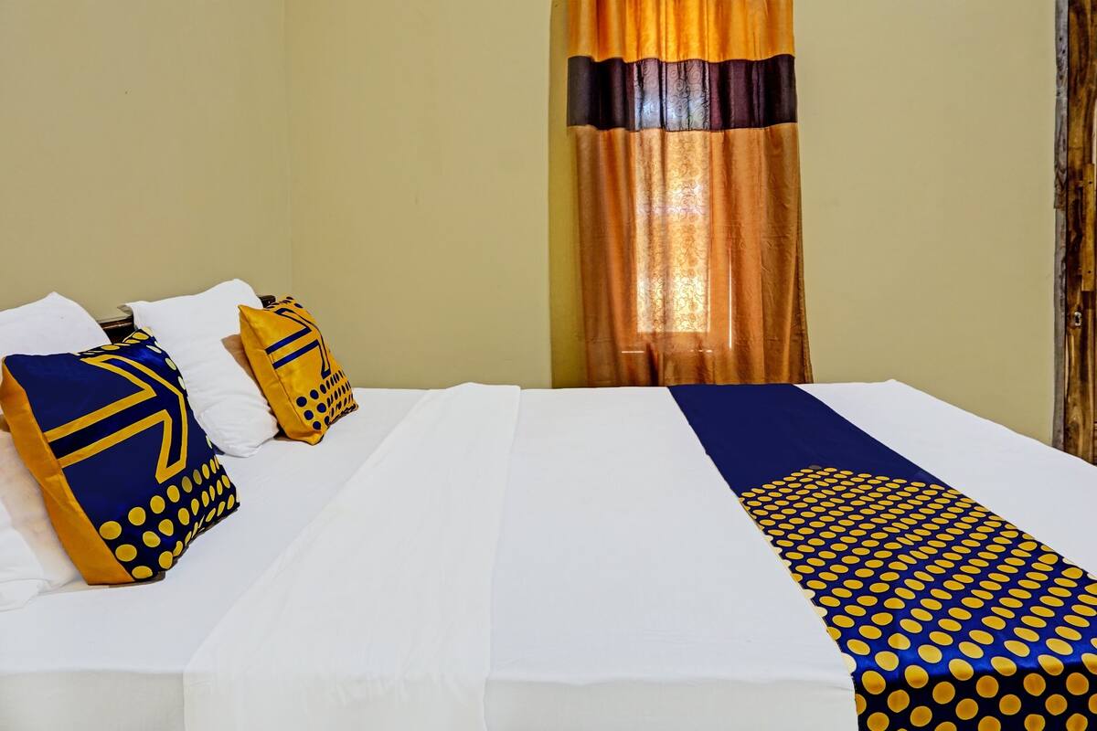 A hotel room with a neatly made bed, a window with curtains, and a bedspread with a geometric pattern.