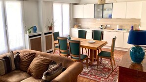 A living room with a brown leather sofa, green chairs, a wooden dining table, and a kitchen in the background. - Centre Paris, Grand Appartement Calme et Lumineux (Paris)