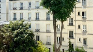 A multi-story building with balconies, a large tree in the foreground, and a clear sky. - Centre Paris, Grand Appartement Calme et Lumineux (Paris)