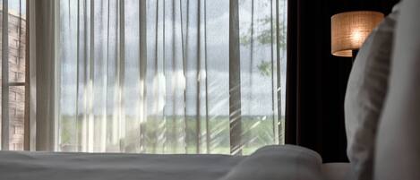 A hotel room with a bed, sheer curtains, and a lamp.