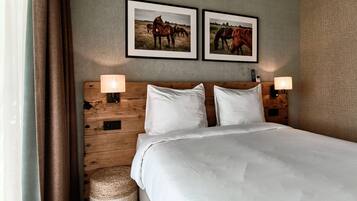 Habitación de hotel con cabecera de madera, dos cuadros enmarcados de caballos, una cama con sábanas blancas, dos lámparas de noche y una cesta tejida.